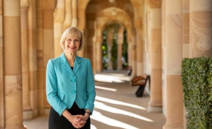 Woman in a blue jacket stands outside a shady sandstone building.